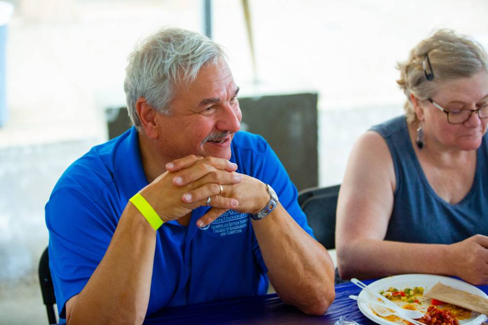 A elderly man wearing a gsvu polo is smiling and sitting next to his wife at the gvsu party